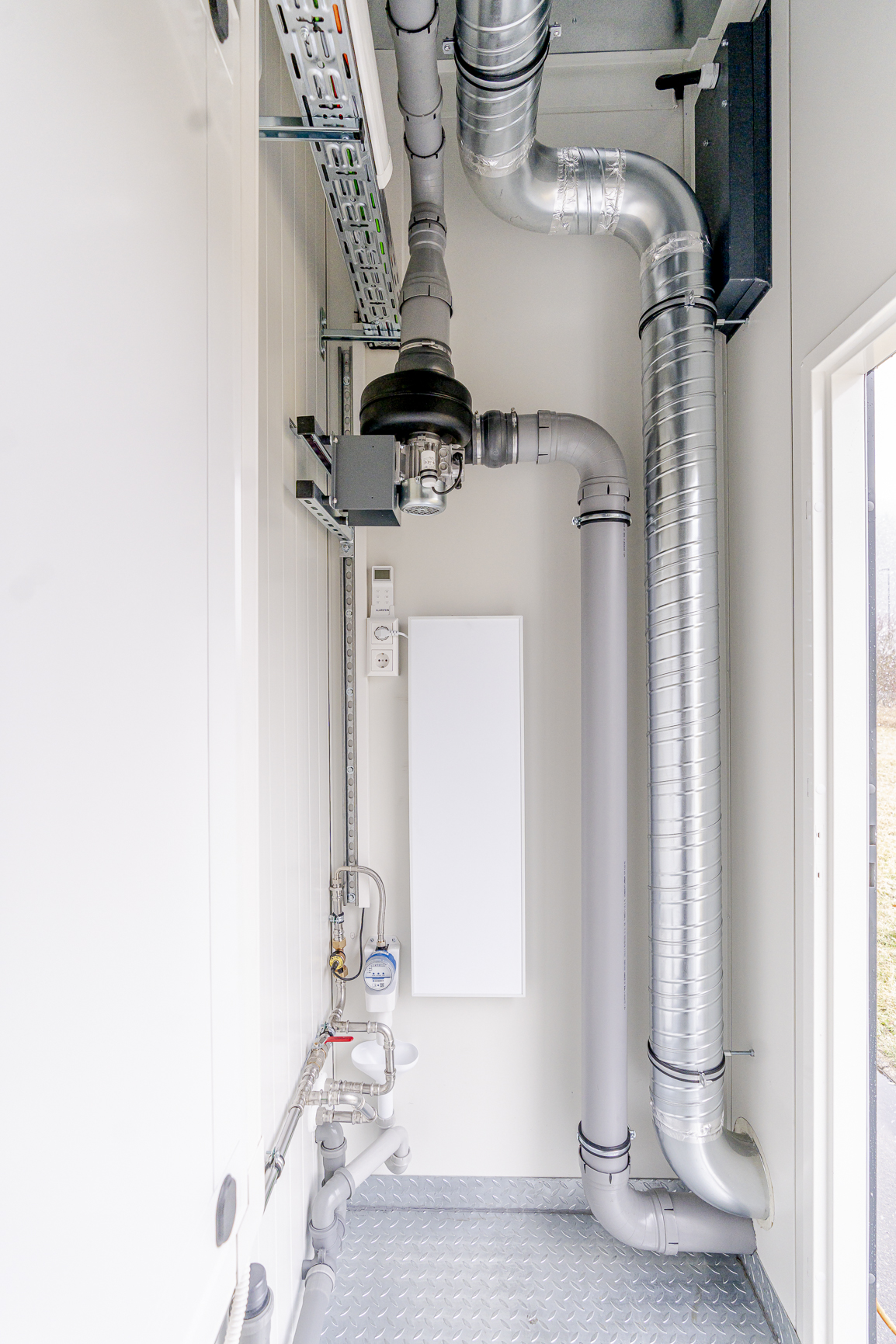 Technikraum-Detail mit Lüftungsrohren, Elektroverteilung und Wasserinstallation